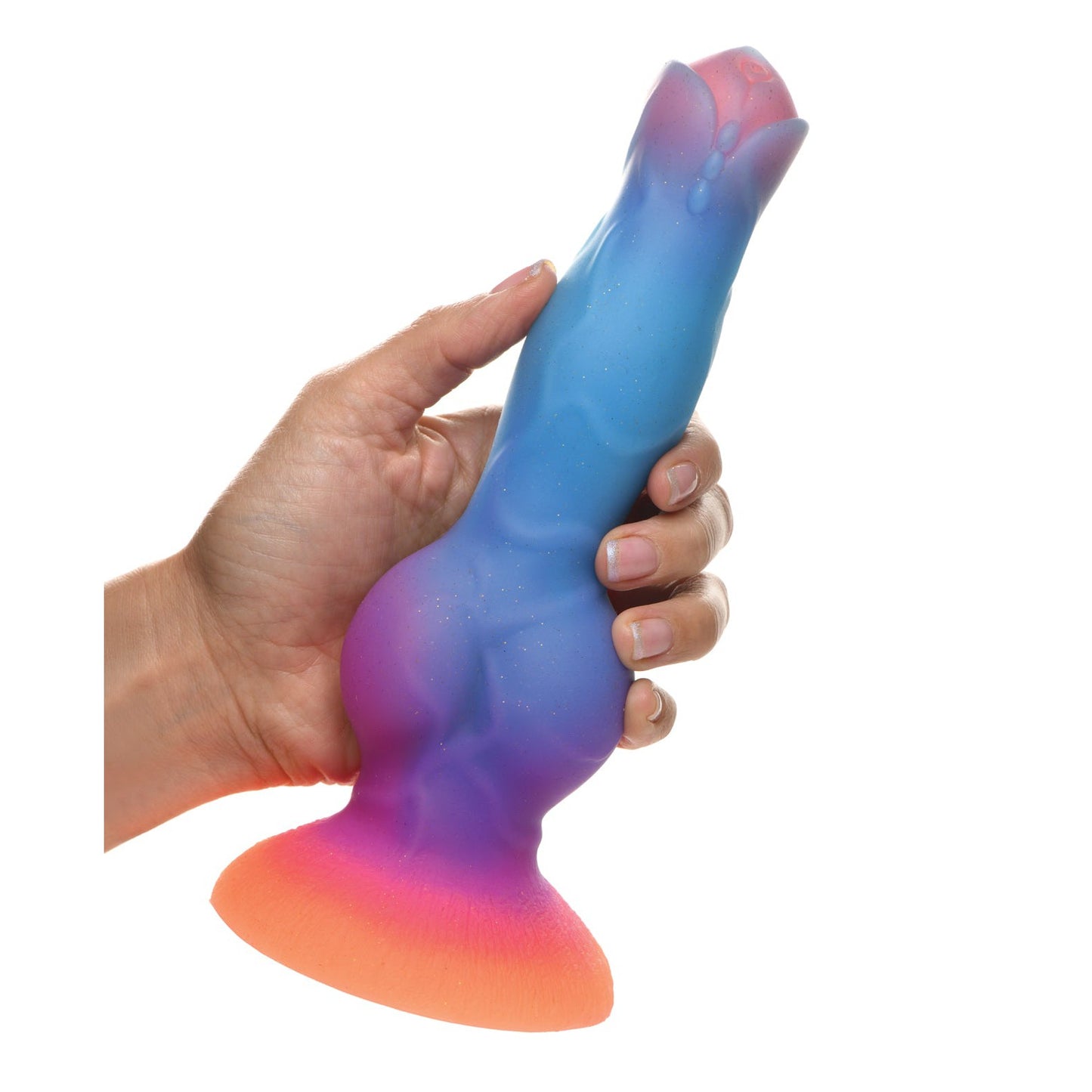 A hand holds the Creature Cocks Space Cock Silicone Alien Dildo, showcasing its glow-in-the-dark, multicolored design. The artistic piece features a wide base and textured surface in shades of blue, purple, pink, and orange.