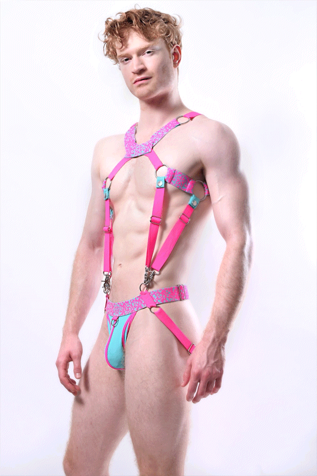 *ssTricks Pixelation Set: neon pink harness with pixel print bands, O-rings and clips joined to an aqua pouch jockstrap, worn by a red-haired man on white.