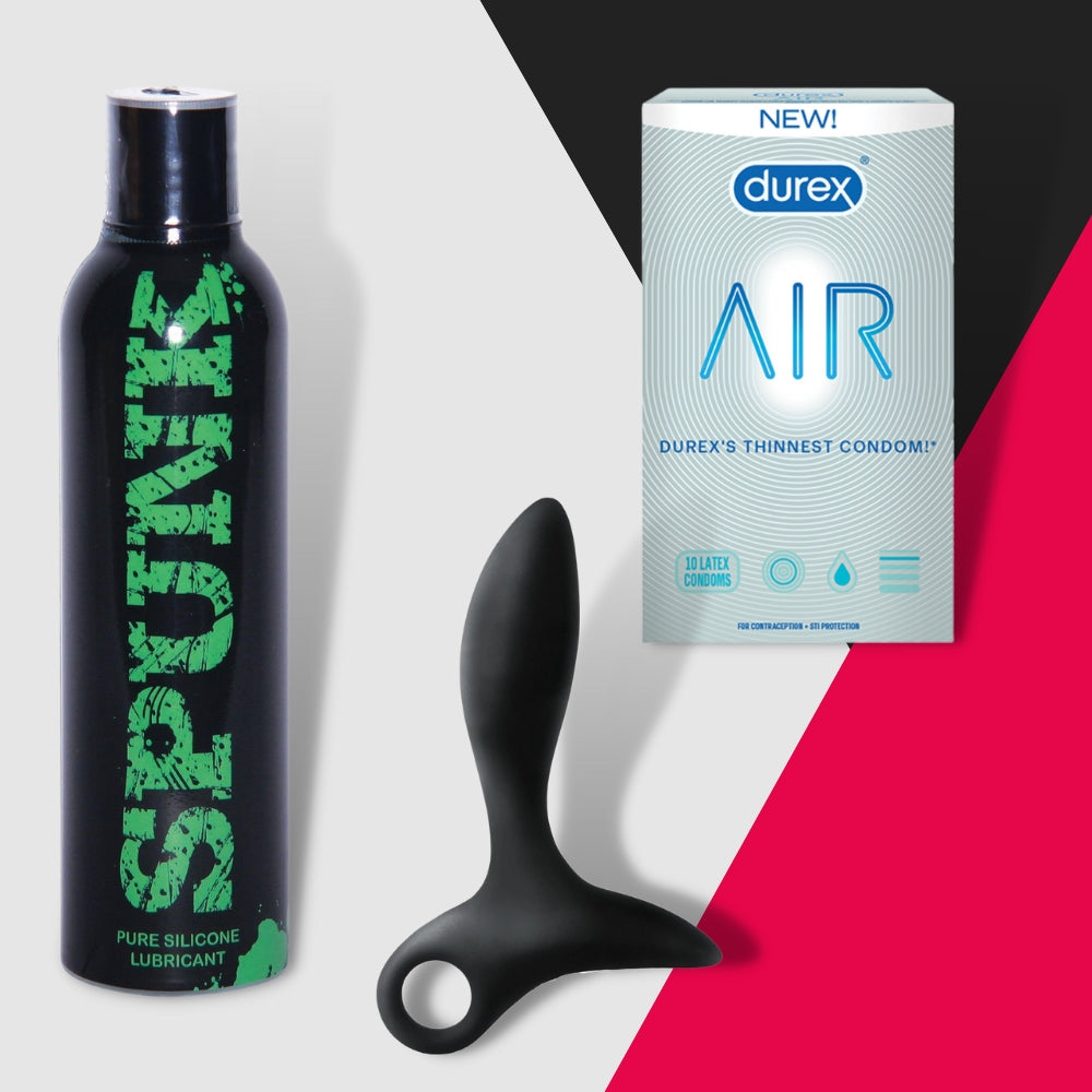 The Just Out Subscription Box from Adams Toy Box features a SPUNK silicone lubricant, a sleek black anal plug, and Durex Air condoms arranged on a modern geometric backdrop in gray, red, and black for an enticing glimpse into pleasure.