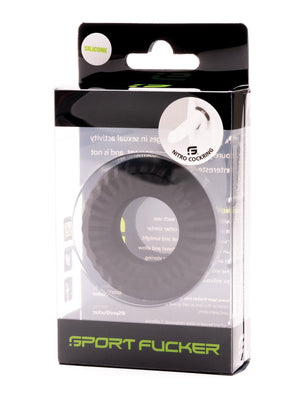 A black silicone cock ring from Sport Fucker is presented in a transparent plastic box featuring white and green text and logos. The rectangular packaging showcases the Sport Fucker Nitro Ring label, combining a sleek design with sporty appeal.