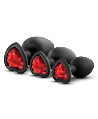 The Blush Luxe Bling Plugs with Gems by Swiss Navy feature four black, heart-shaped pieces with red gem-like accents, arranged from small to large. Made of smooth material and body-safe silicone, they are artistically displayed against a plain background.