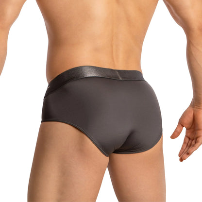 A person wearing Agacio Sheer Boxer Briefs with Pouch in dark gray stands with their back turned. The smooth, stretchy fabric offers a snug fit and contoured design. A slightly shiny waistband contrasts the matte finish, enhancing comfort and support.