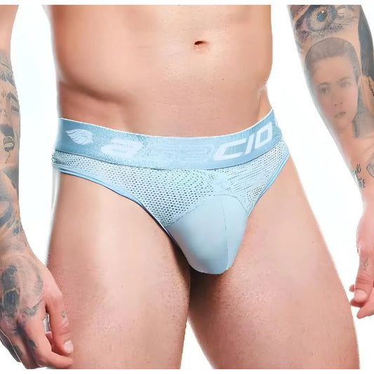 A person wears light blue Agacio Thong for Men, featuring a mesh design and wide waistband, with tattoos visible on their arms. The plain white background highlights the minimalist style of the Agacio brand.