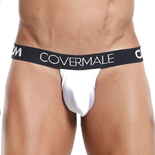 A person wearing a white Cover Male Slip Thong with a black waistband displaying the Cover Male brand name is showcased against a plain background, highlighting minimalist design that emphasizes style and comfort with its revealing back and sleek lines.