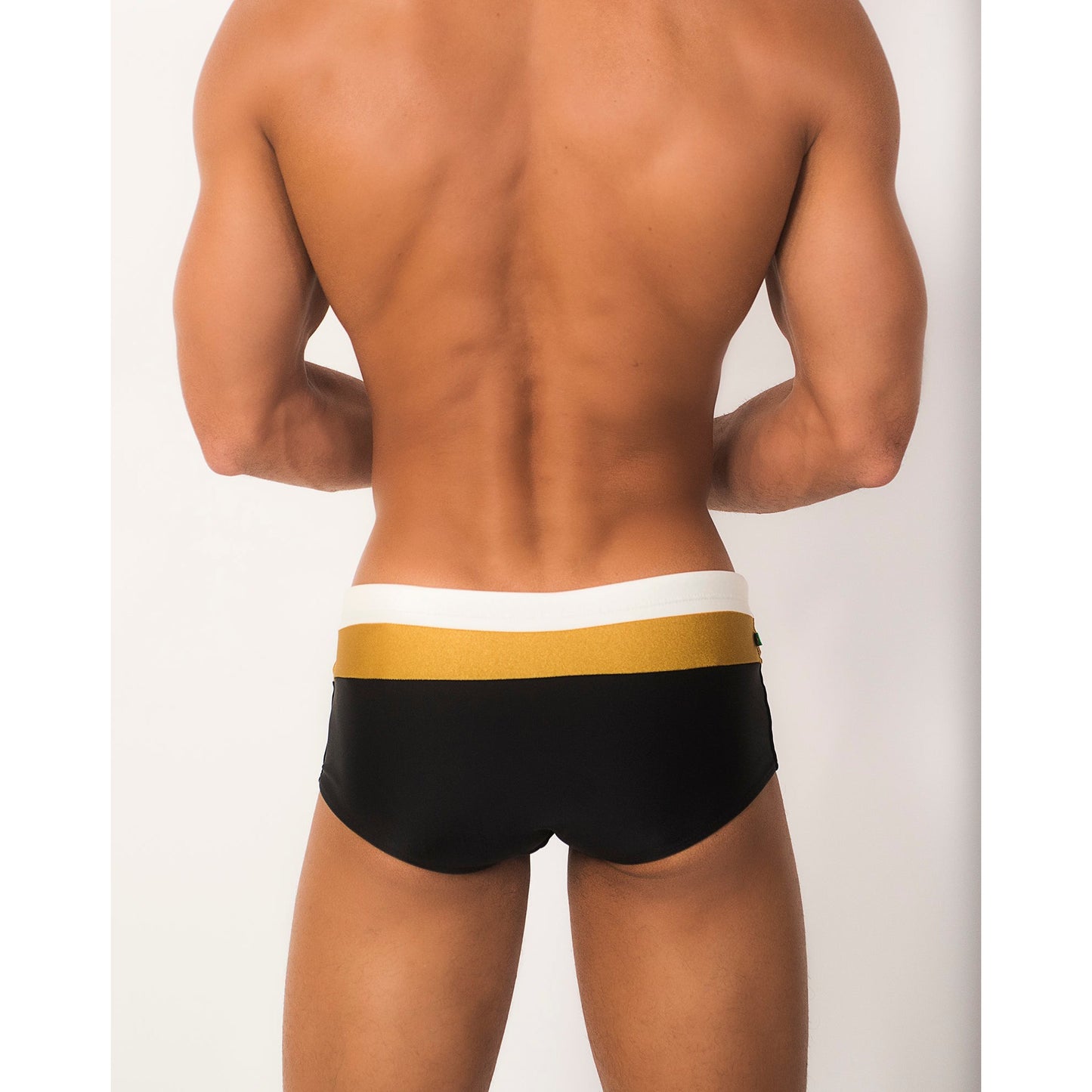 A person stands against a light background, wearing the luxurious Belmont Trio Sunga designer swim shorts by CA-RIO-CA Sunga Co., featuring a wide yellow and white waistband. Their arms are slightly bent at the elbows.