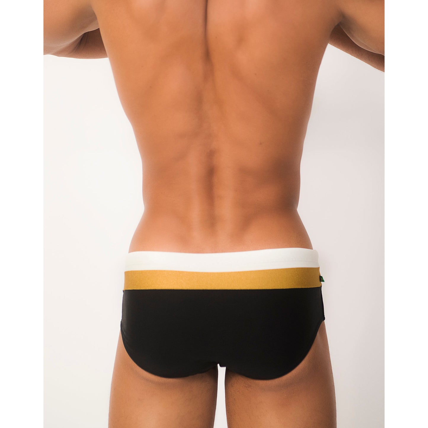 A rear view shows someone in Belmont Trio Sunga shorts by CA-RIO-CA Sunga Co., featuring a black design with a white and gold waistband, made from premium materials. The backdrop is plain white.