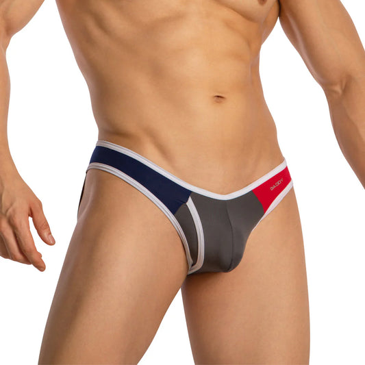 A muscled individual models the Daddy Provocative Rear Exposing Jockstrap, featuring a color-blocked design in gray, blue, and red. The look is highlighted by a Daddy brand logo on the waistband, with the face remaining unseen.