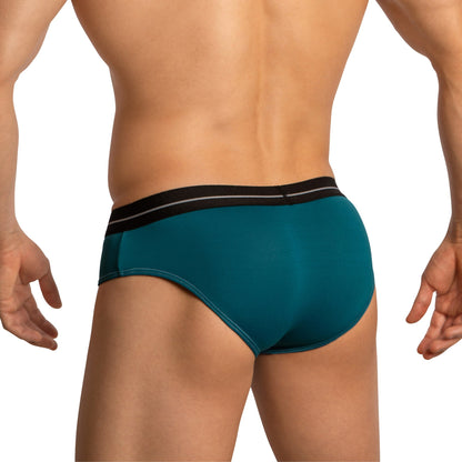 A person, back facing the camera, showcases Feel Thongs for Men in teal with a black waistband. The luxurious fabric blend and contour pouch design are highlighted against the white background, emphasizing the fit and color of this Feel brand underwear.