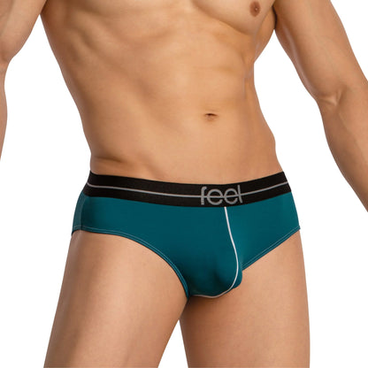 A torso clad in Feel Thongs for Men is highlighted, showcasing teal fabric with a black and white Feel waistband. Made from a luxurious blend, these thongs enhance comfort and support with their contour pouch design, while the face remains unseen.