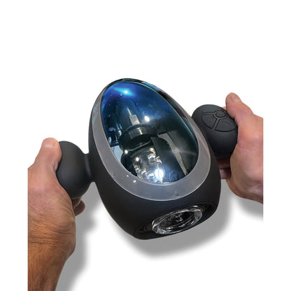 A person holds a sleek, oval-shaped MSTR B8 Blast Off Stroker, featuring a transparent blue cover showing internal mechanisms. The black device includes dual grips, various thrusting modes with front propeller-like action, and is controlled by a small round device in the right hand.