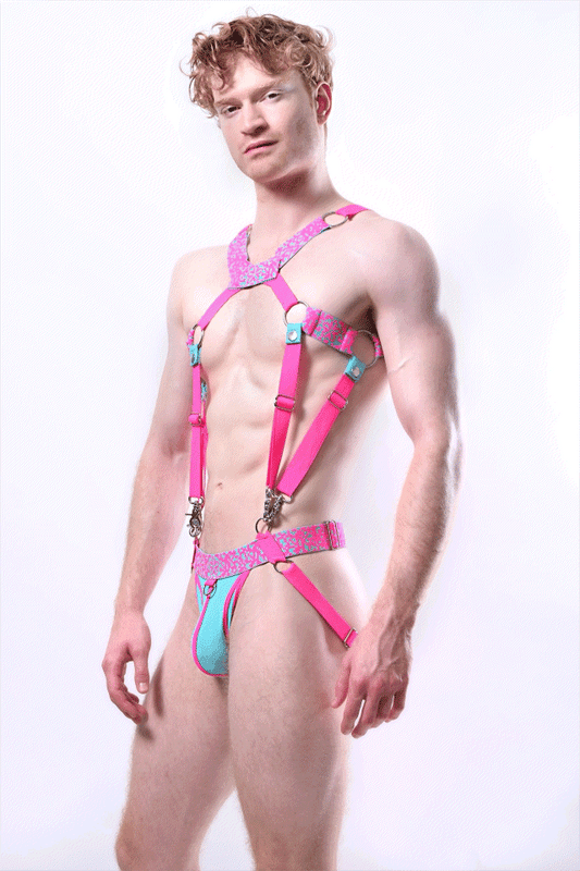 *ssTricks Pixelation Set: neon pink harness with pixel print bands, O-rings and clips joined to an aqua pouch jockstrap, worn by a red-haired man on white.